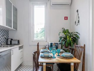 Modern kitchen with a wooden dining table set for a meal, tiled floors, and a large window letting in natural light