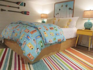 Cheerful beach-themed bedroom with a colorful surfboard patterned quilt, striped rug, and vibrant coastal decor, evoking a playful seaside ambiance.