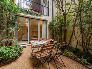 Patio dining area in a secluded courtyard with lush greenery and a modern glass backdoor in Lisbon