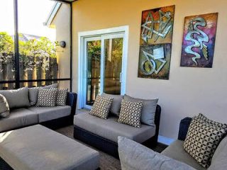 Cozy outdoor patio with modern grey wicker sofas and decorative pillows, complemented by abstract artwork, perfect for relaxation under open skies.