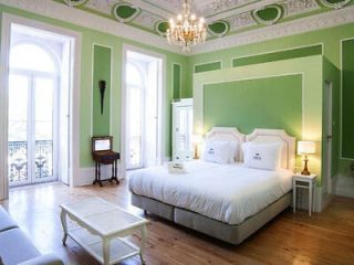 Elegant bedroom with green walls, ornate white moldings, and large windows leading to a classic wrought-iron balcony