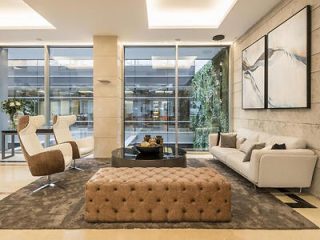 Luxurious hotel lobby with modern furnishings, a large tufted ottoman, sleek white sofas, and a striking black and white abstract painting.