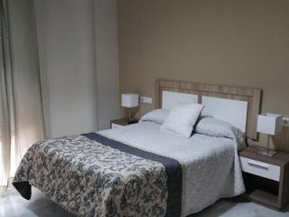 Simple and elegant bedroom with a beige headboard, grey and white bedding, matching nightstands with lamps, and soft curtains.