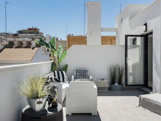 Contemporary rooftop patio with woven outdoor furniture, potted plants, and a view of surrounding buildings