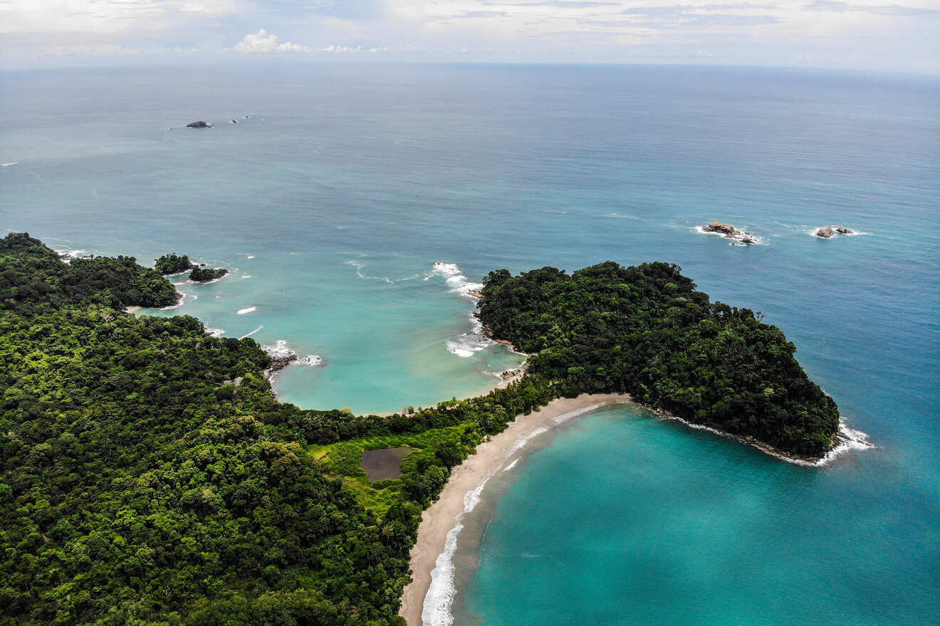 Aerial view of a tropical coastline with dense green forest, sandy beaches, and turquoise waters extending into the horizon.