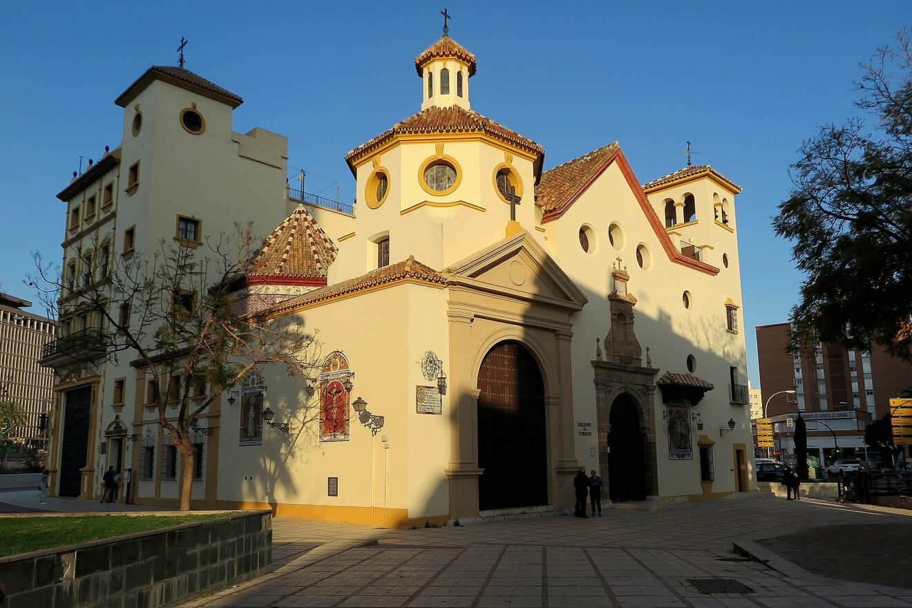 Traditional church in Malaga with a yellow and white facade, ornate red-tiled dome, and intricate mosaics, set against a clear sky in an urban street scene.