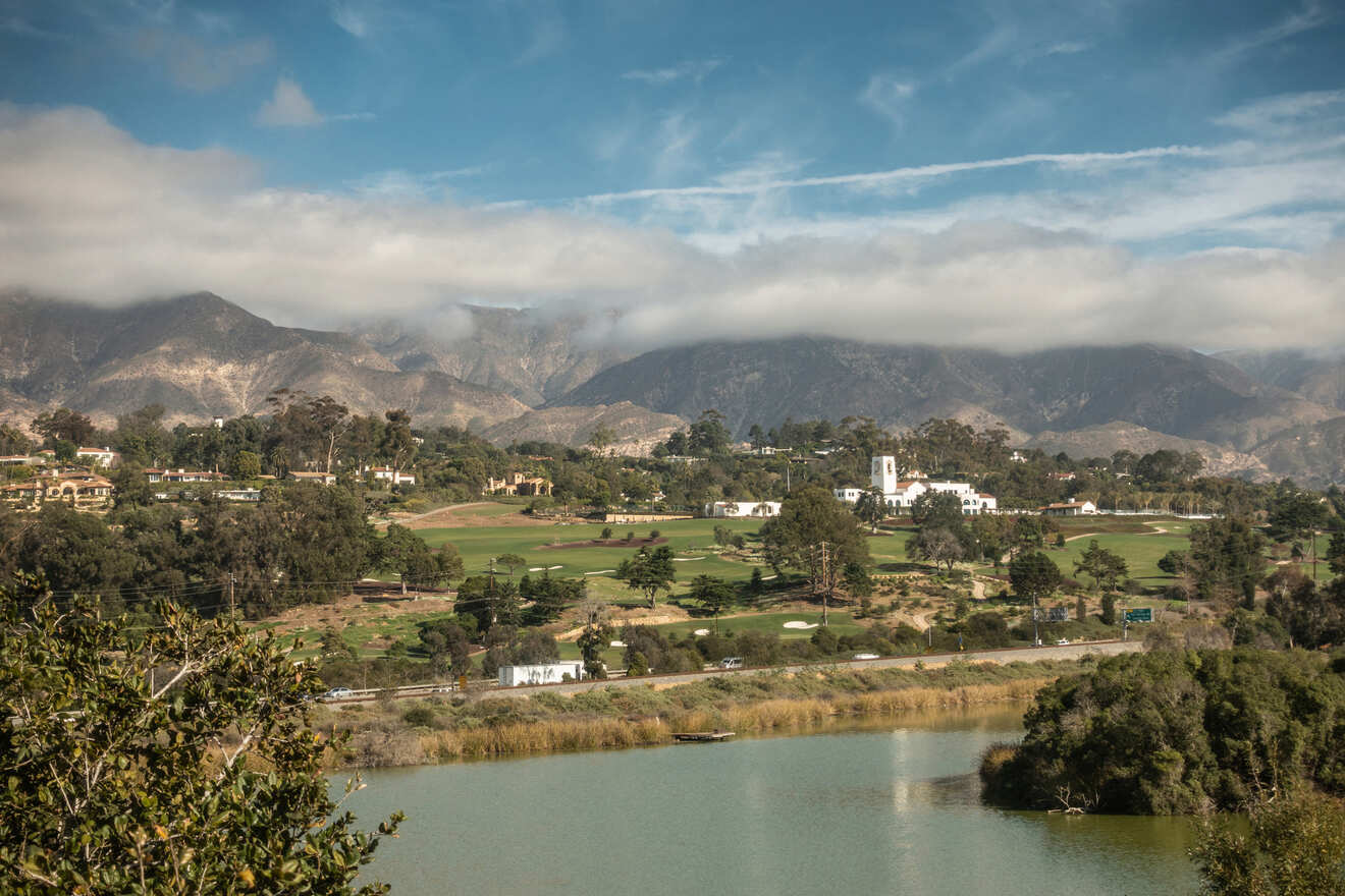 A tranquil lake in the foreground with a panoramic view of Santa Barbara's lush landscape and cloud-kissed Santa Ynez Mountains in the distance