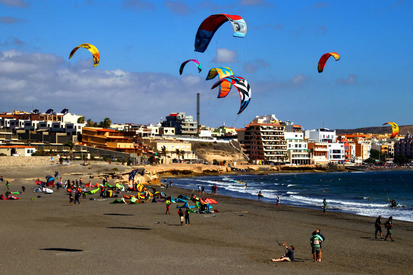 A beach bustling with activity, showcasing colorful kitesurfing gear against a backdrop of a coastal town