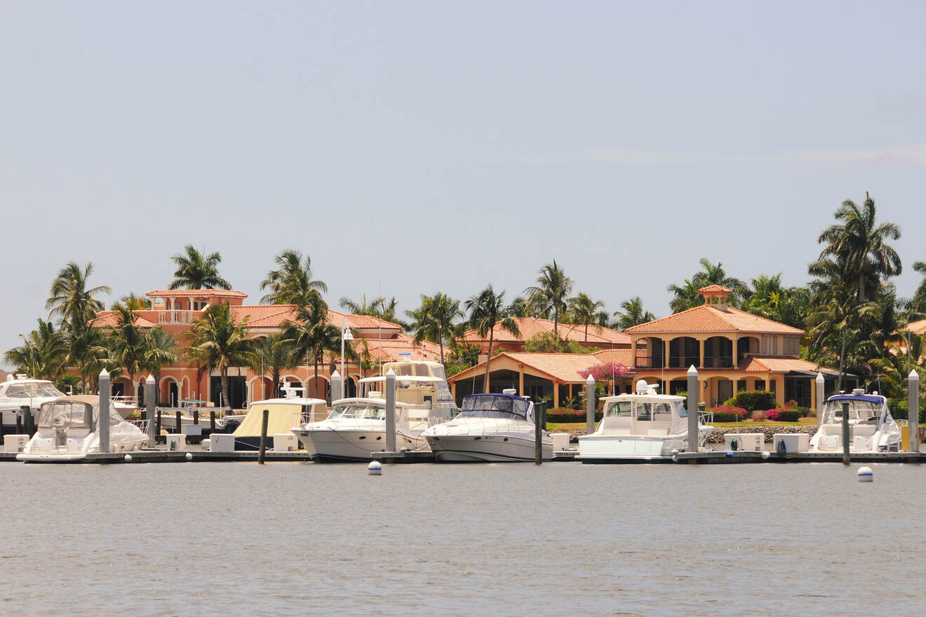 Luxurious waterfront homes with terracotta roofs and private docks housing various yachts and boats, reflecting an opulent lifestyle in a serene coastal setting