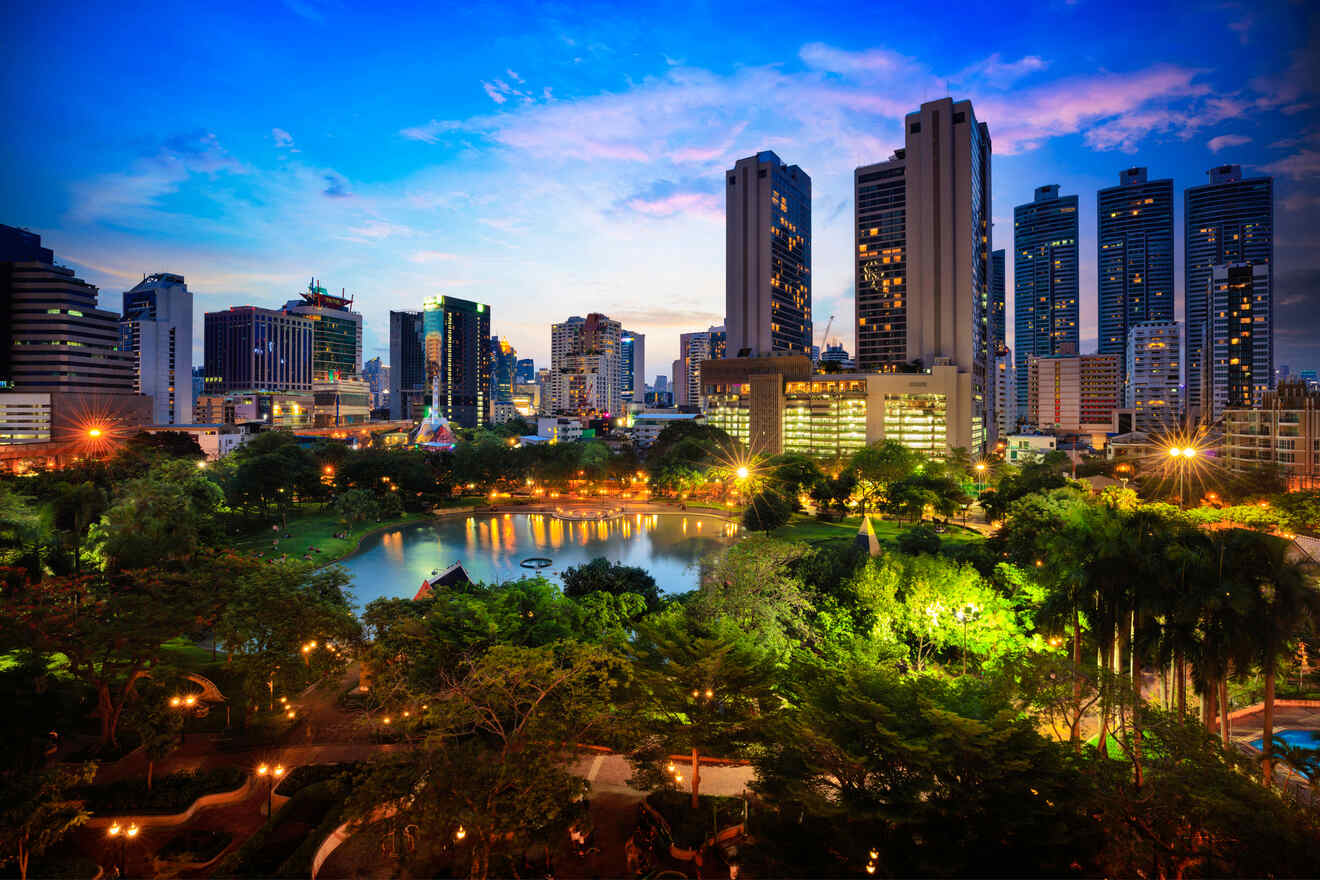 Twilight view of a park in Panama City with illuminated walkways, a serene pond, and a skyline of lit-up skyscrapers reflecting on the water surface.