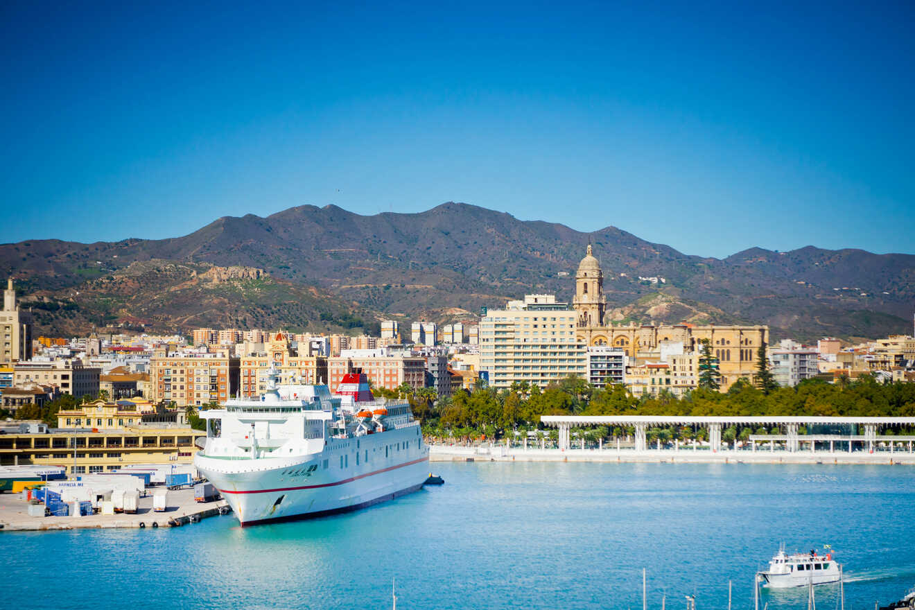 Scenic view of a port city with a large cruise ship docked, surrounded by modern architecture, with mountains in the background under a clear blue sky