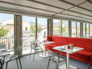 A restaurant with red couches and tables overlooking a city.