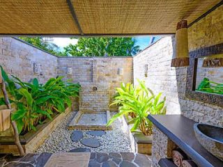 A private outdoor bathroom with natural stone walls, lush green plants, and an open-air shower area