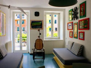 Art-filled room with vibrant framed pictures, twin beds, and a view out to the colorful buildings 