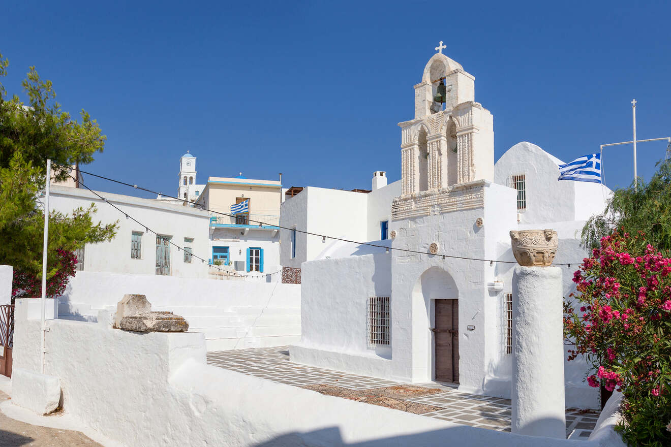 Traditional white Greek church with a bell tower surrounded by bougainvillea flowers