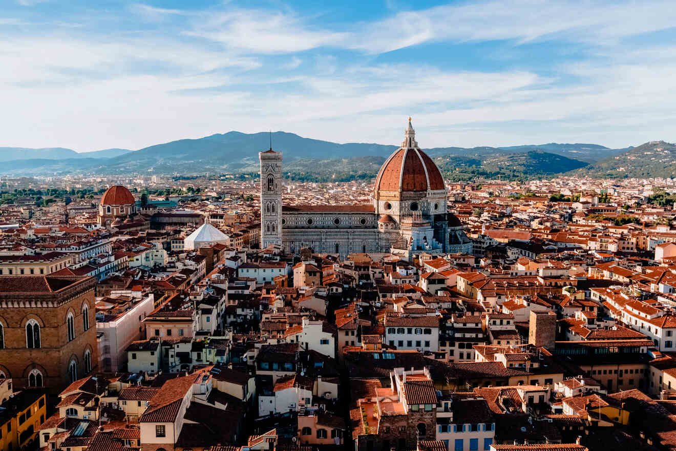 Panoramic view of Florence, Italy, showcasing the iconic Duomo with its red-tiled dome, the Giotto's Campanile, and the historic urban architecture spread beneath a clear blue sky