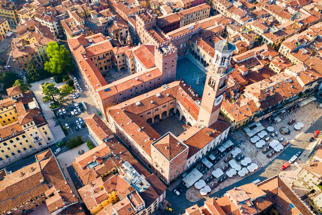 Aerial view of the historic center of Verona, Italy, showcasing the terracotta rooftops, the Lamberti Tower, and Piazza delle Erbe with its market stalls