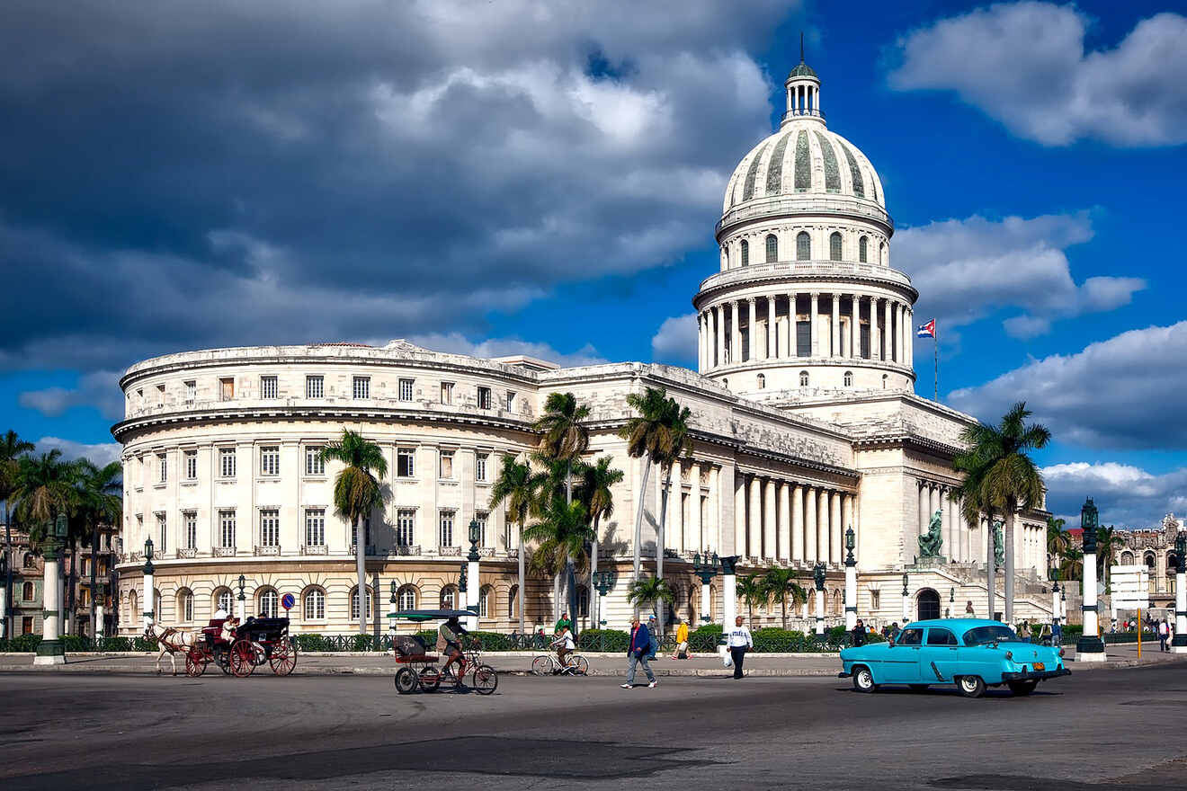 A neoclassical building with a dome under a cloudy sky, with vintage cars and horse-drawn carriages on the street in front.