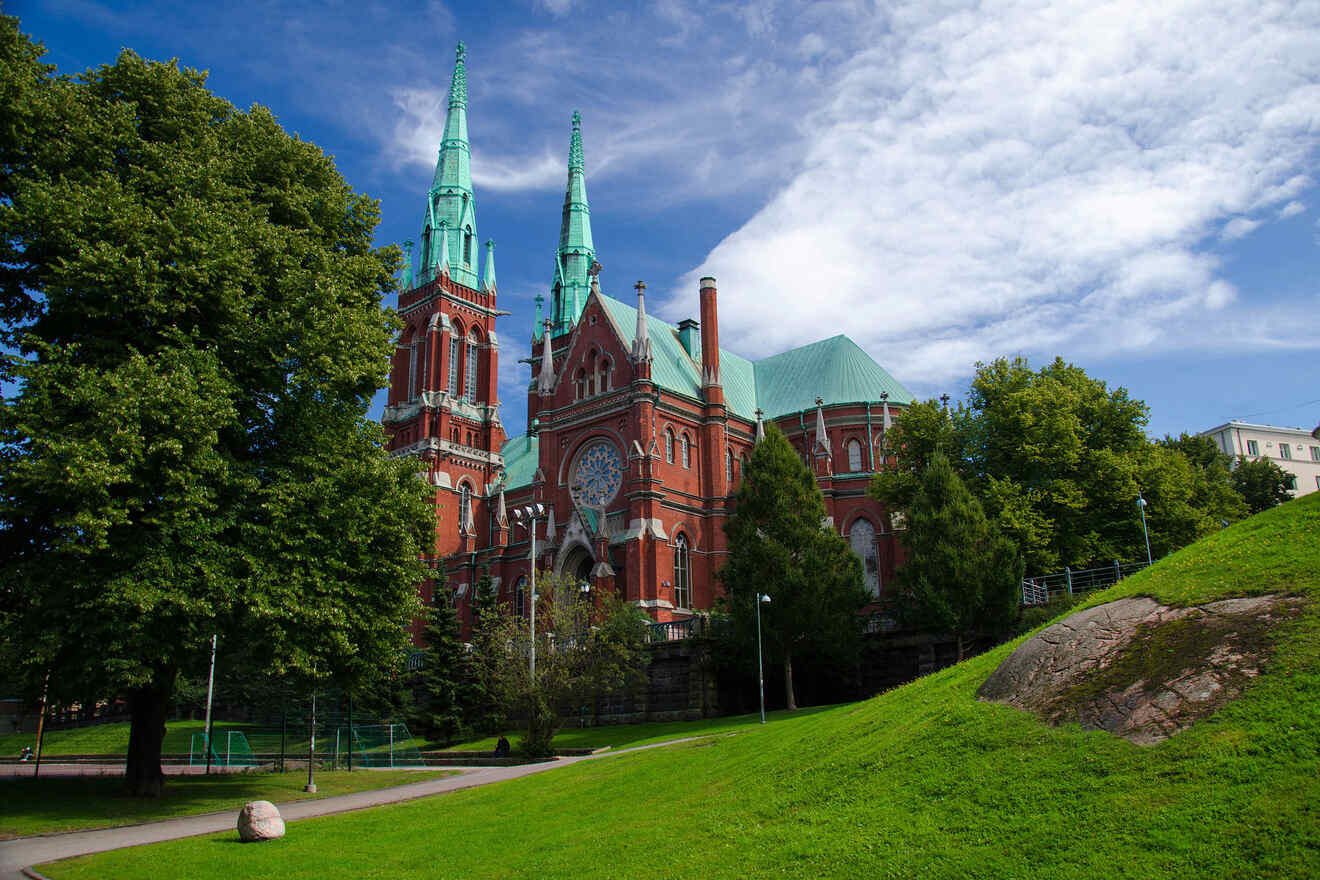 The historic red-brick Johanneksenkirkko church in Helsinki surrounded by lush green trees under a clear blue sky