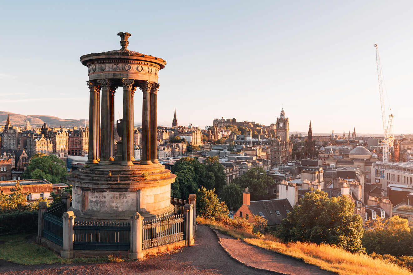 The warm light of the setting sun bathes the Dugald Stewart Monument and the Edinburgh skyline, capturing a serene moment with the city's historic buildings and soft pastel sky