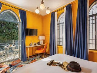 Hotel room with vibrant yellow and blue decor, large windows, and a view of the outdoor surroundings.