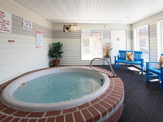 Indoor hot tub area with tiled walls, a round brick-lined hot tub, safety signs, and blue benches on a black rubber mat floor.