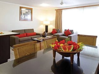 A spacious living room in a holiday apartment with red and beige sofas, a large glass-top dining table with a fruit bowl