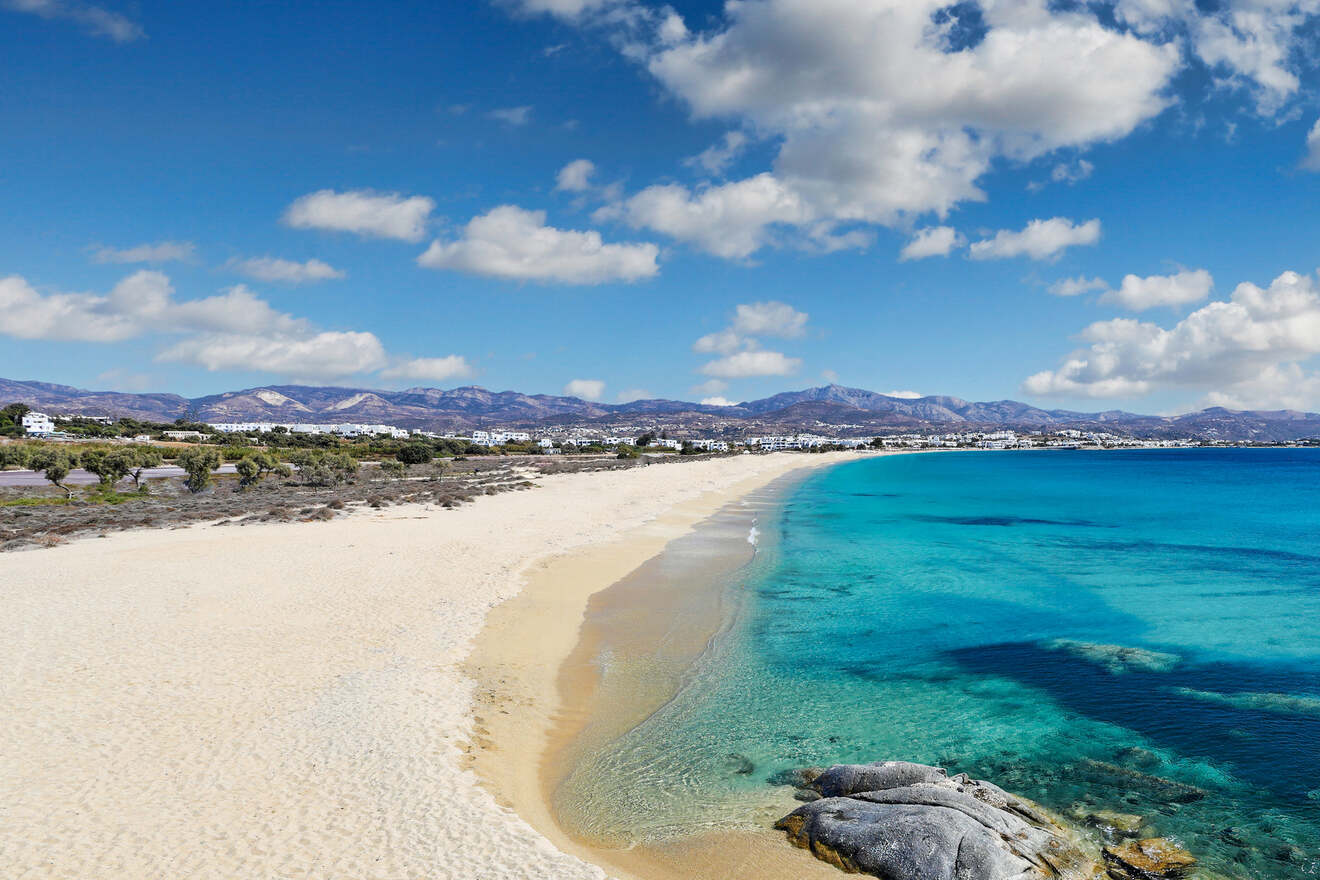 A pristine sandy beach with turquoise waters, set against a backdrop of mountains and a partly cloudy sky.