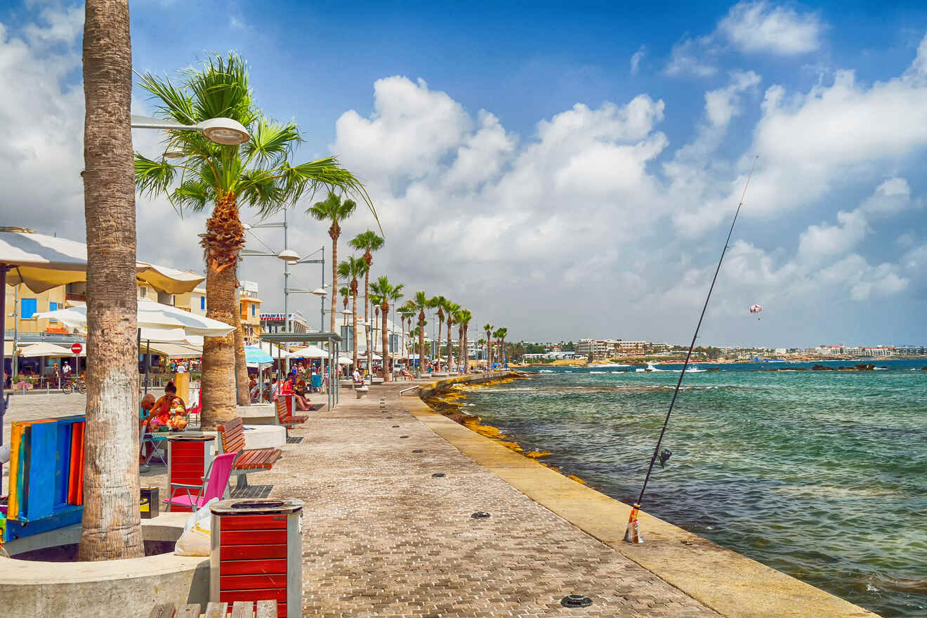 Vibrant seaside promenade in Paphos, Cyprus, with palm trees, outdoor cafes, and a fishing rod overlooking the turquoise sea, embodying a relaxed coastal ambiance