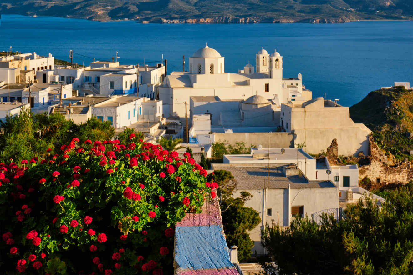 Breathtaking view of Greek architecture in Milos and red geraniums with the sea and mountains in the distance