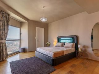 Elegant hotel room with a grey upholstered bed, a large window, and soft natural lighting.