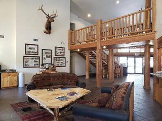 Lobby with rustic wooden furniture, a mounted deer head on the wall, staircase, and framed pictures.