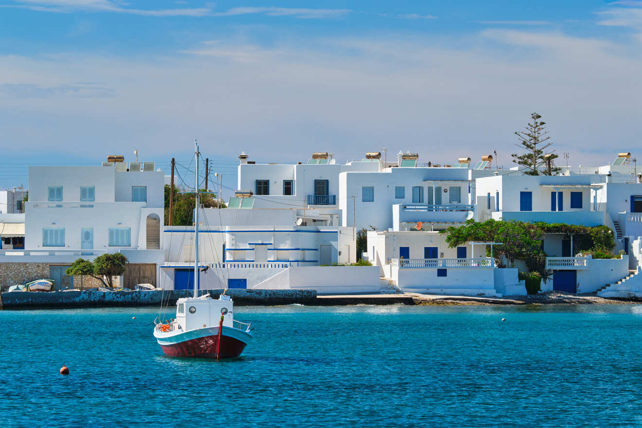 A tranquil harbor scene with a red and white boat moored in front of white Greek houses by the sea