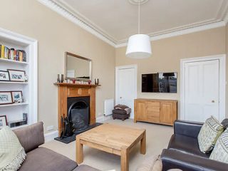 A spacious living room with a neutral color scheme, featuring a fireplace, wooden furniture, a large TV, and cozy sofas