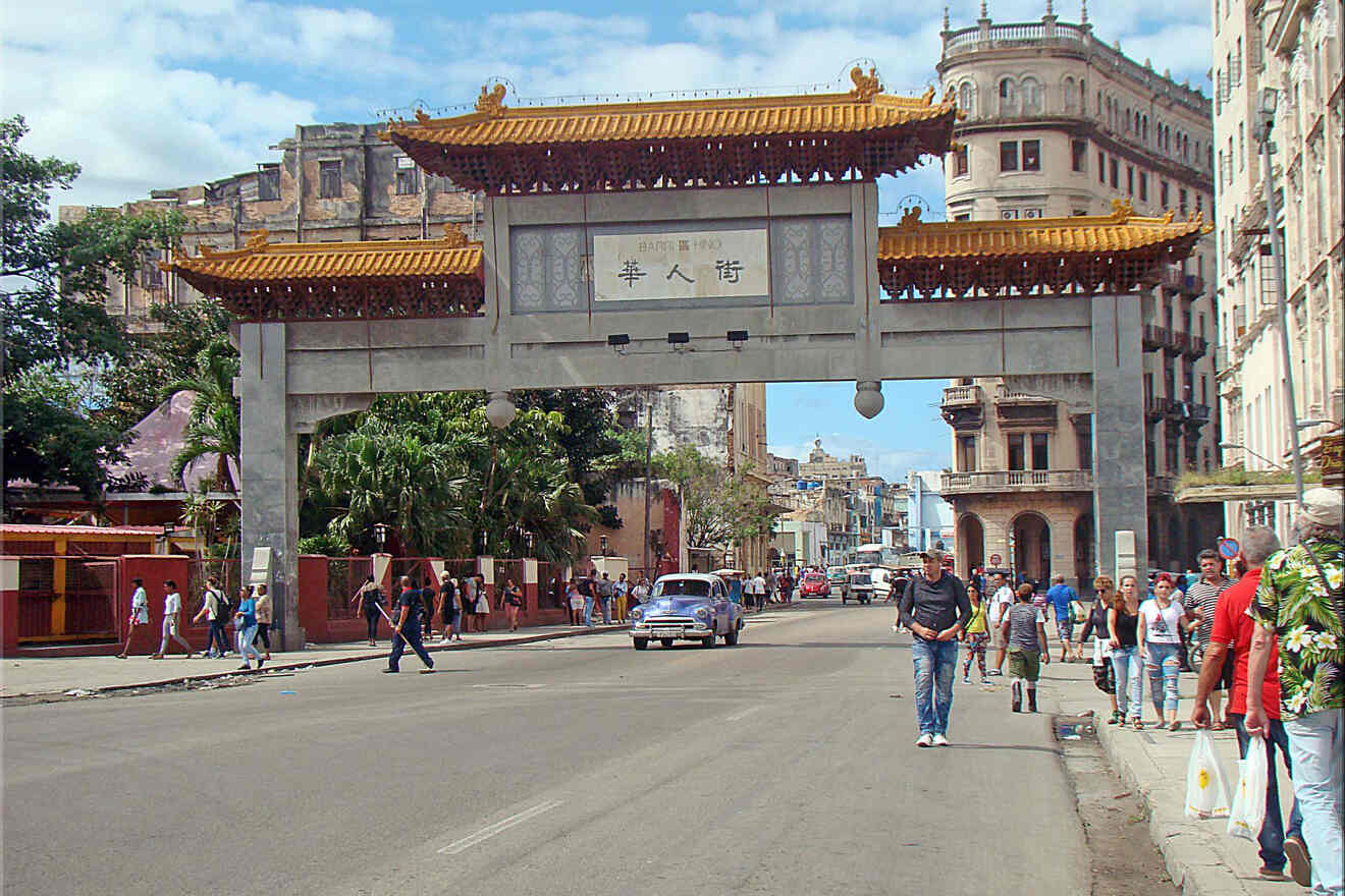 A street scene in Havana, Cuba, featuring the entrance gate of Chinatown, lined with pedestrians, cars, and surrounding buildings.