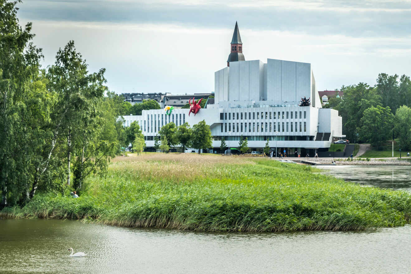 Finlandia Hall, a modernist white building in Helsinki, overlooking a tranquil waterside setting with greenery and a floating red sculpture