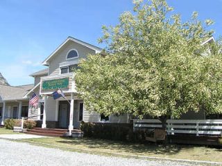 A two-story building with a large tree in front, featuring a sign that reads "Welcome Center." American and state flags are displayed.