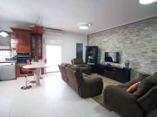 Modern apartment living room with tiled flooring, stone accent wall, and open-plan kitchen.