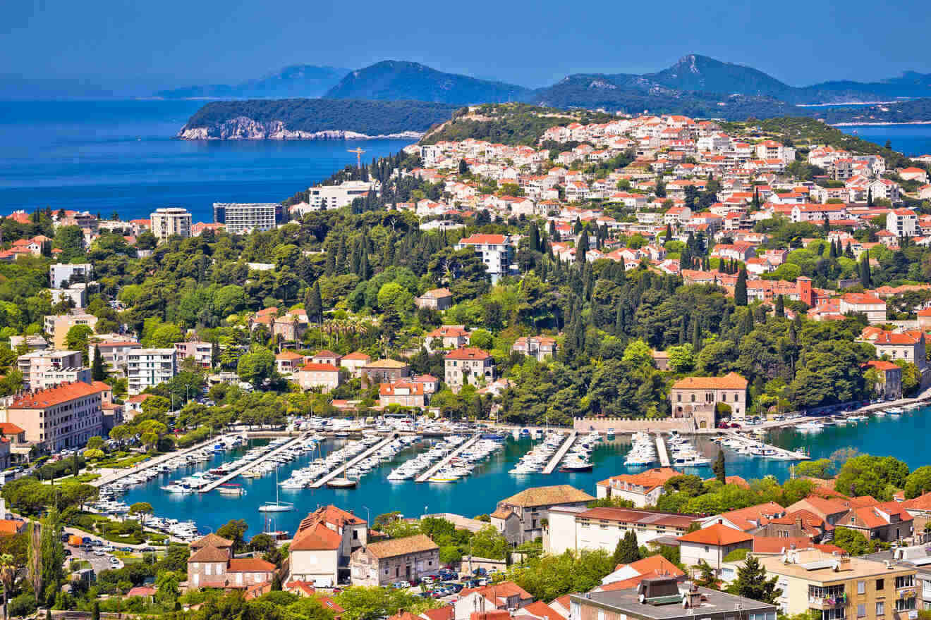 Panoramic view of Dubrovnik's coastline with lush greenery, red rooftops, and the serene blue Adriatic Sea