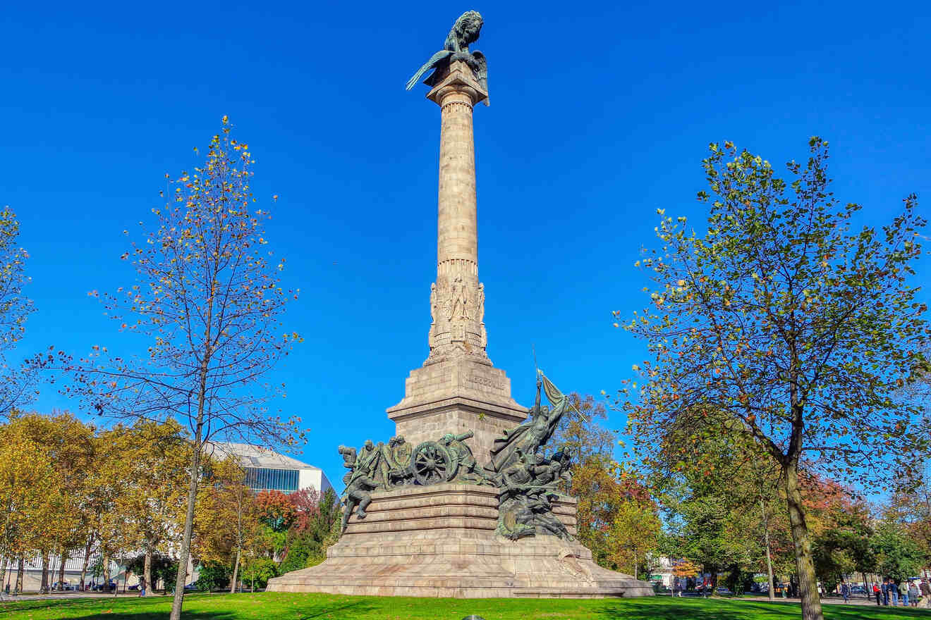 Monumental column of Porto, Portugal, soaring high with intricate sculptures at its base, set in a park with autumnal trees