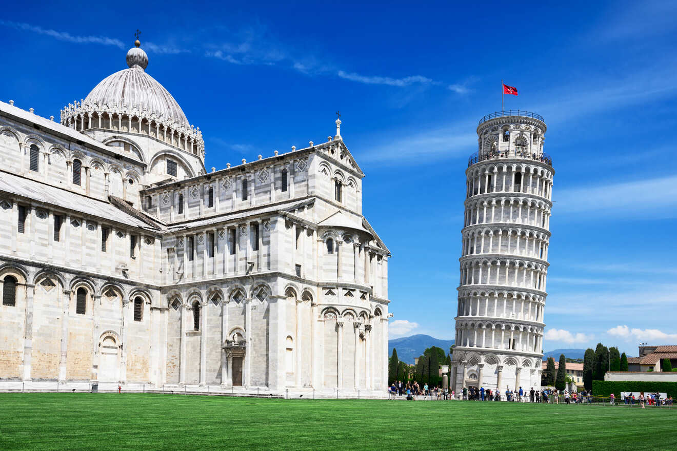 The Pisa Cathedral and the Leaning Tower of Pisa on a bright day, showcasing the architectural beauty of the Romanesque buildings against a vivid blue sky with green lawns in the foreground