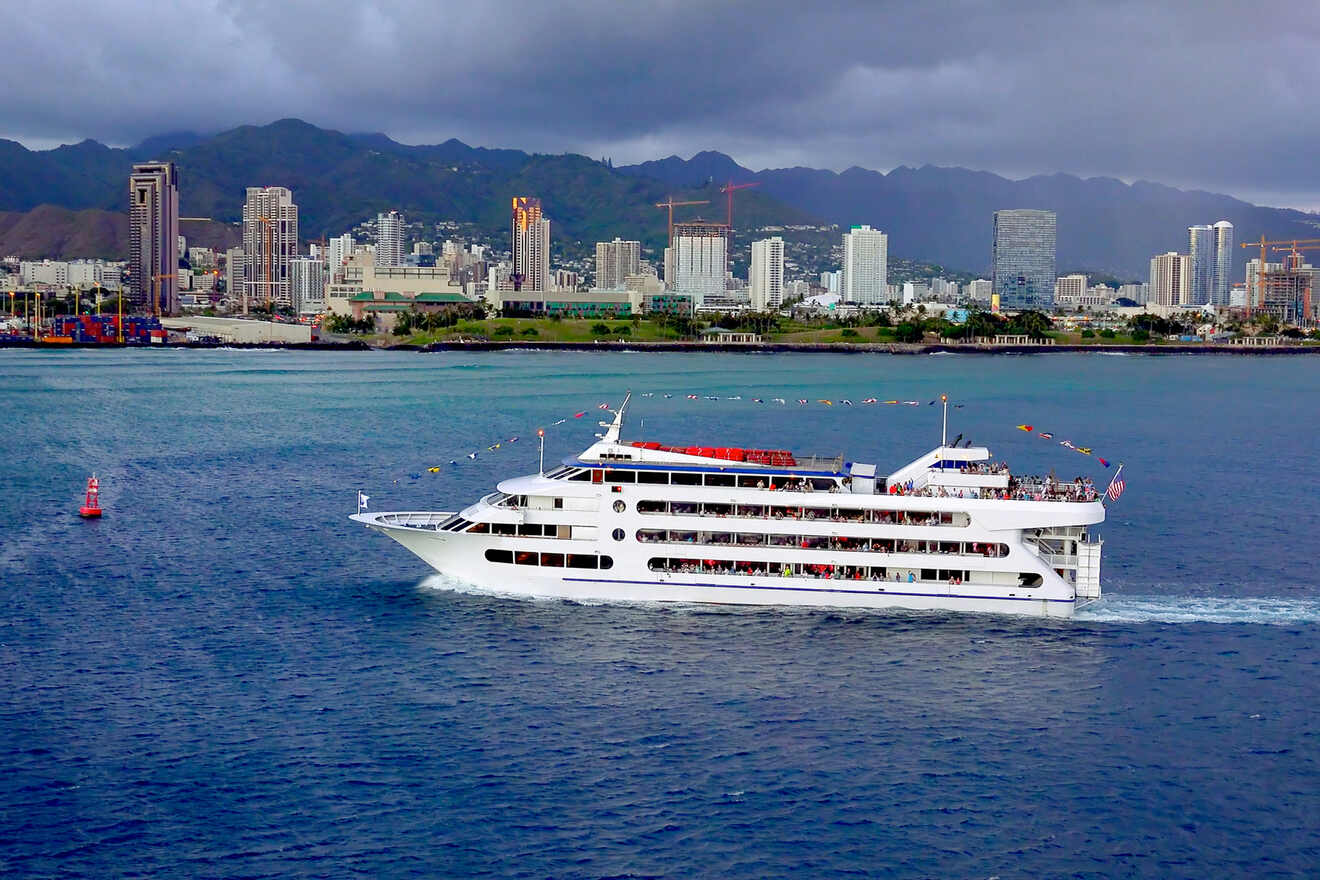 A white cruise ship sails near a city skyline with mountains in the background under a cloudy sky.