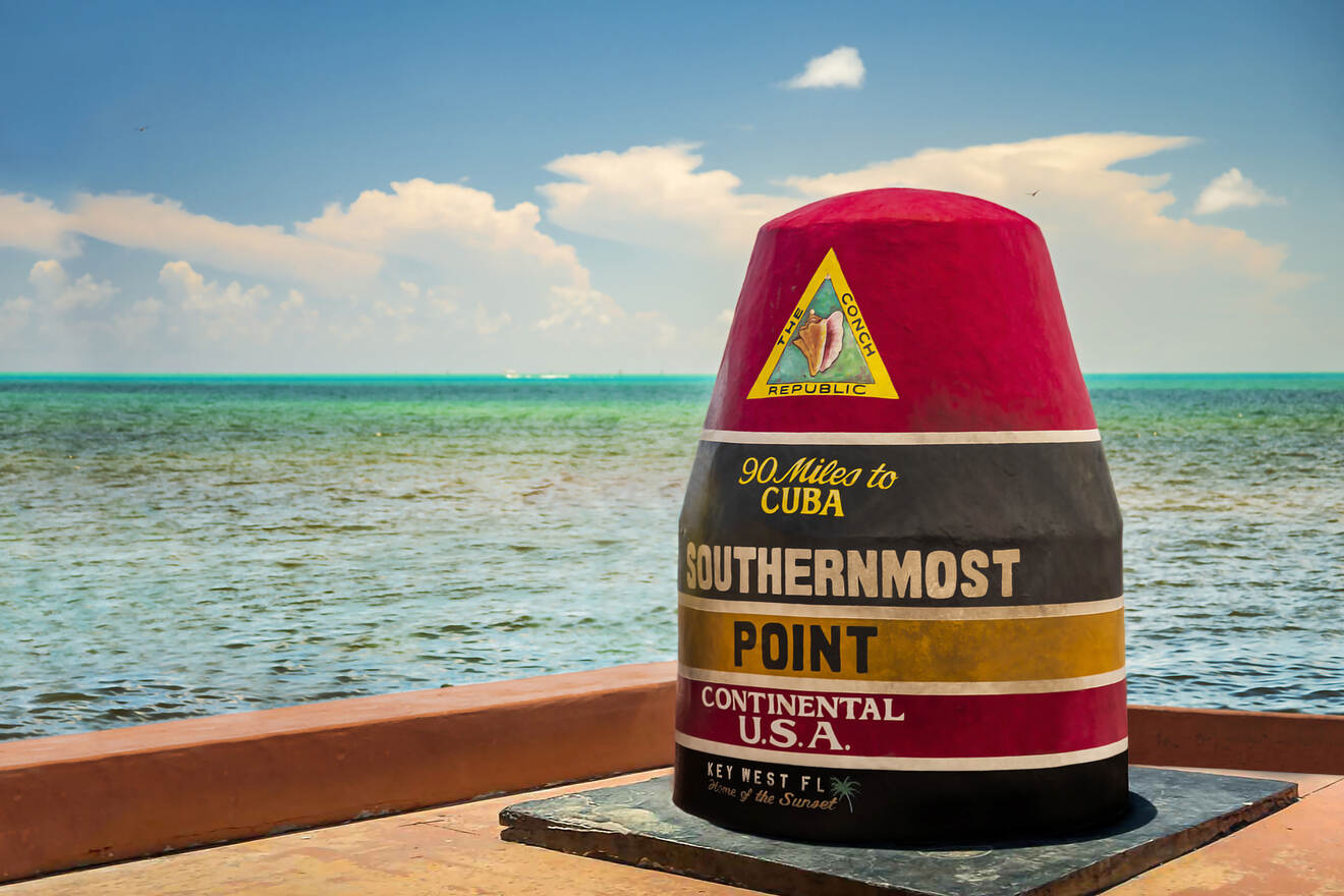 The iconic red, black, and yellow 'Southernmost Point Continental U.S.A.' monument in Key West, with the ocean in the background and clear blue skies