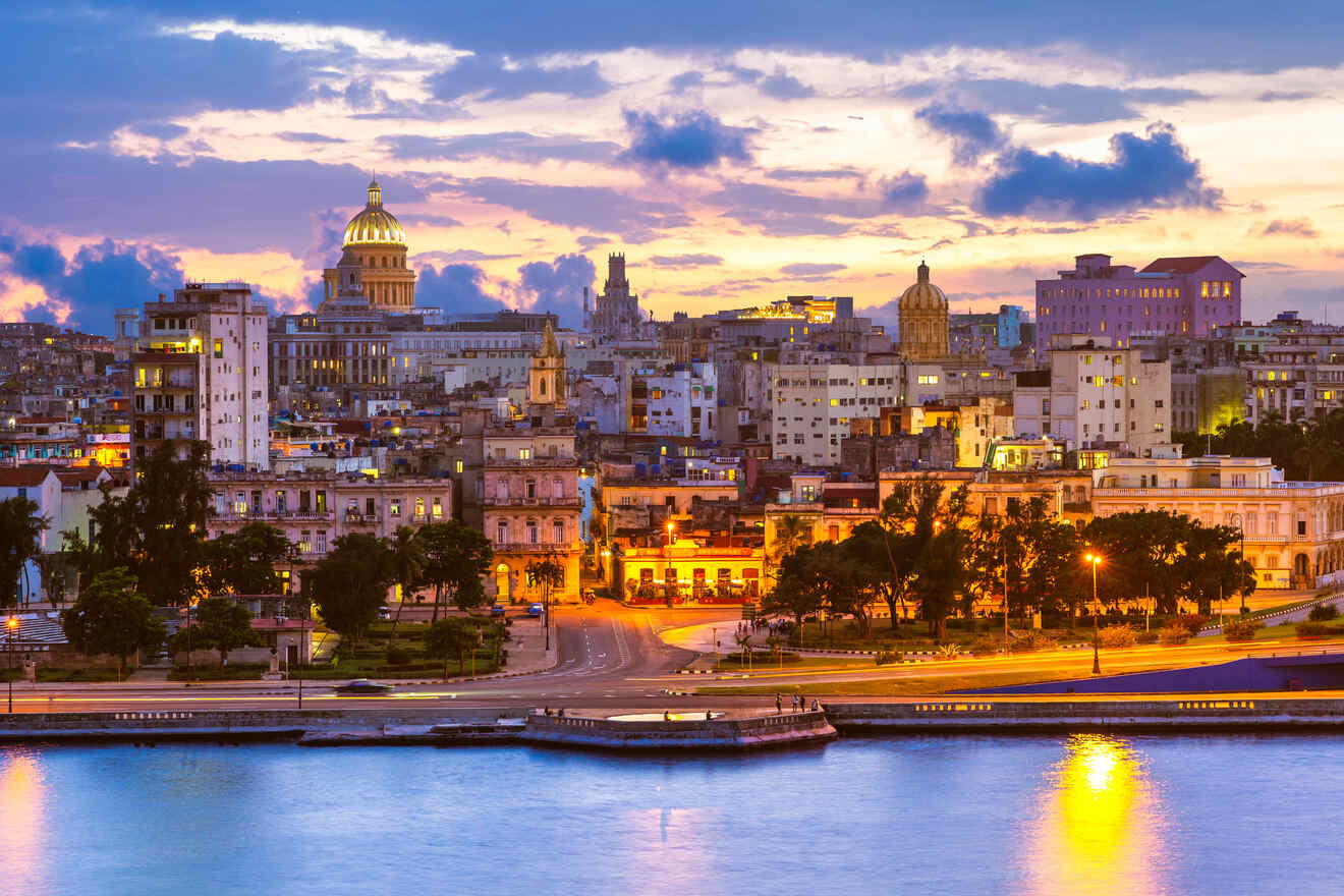 A cityscape of Havana, Cuba at sunset, featuring illuminated buildings, a prominent domed structure, and a riverfront with reflections of lights on the water.