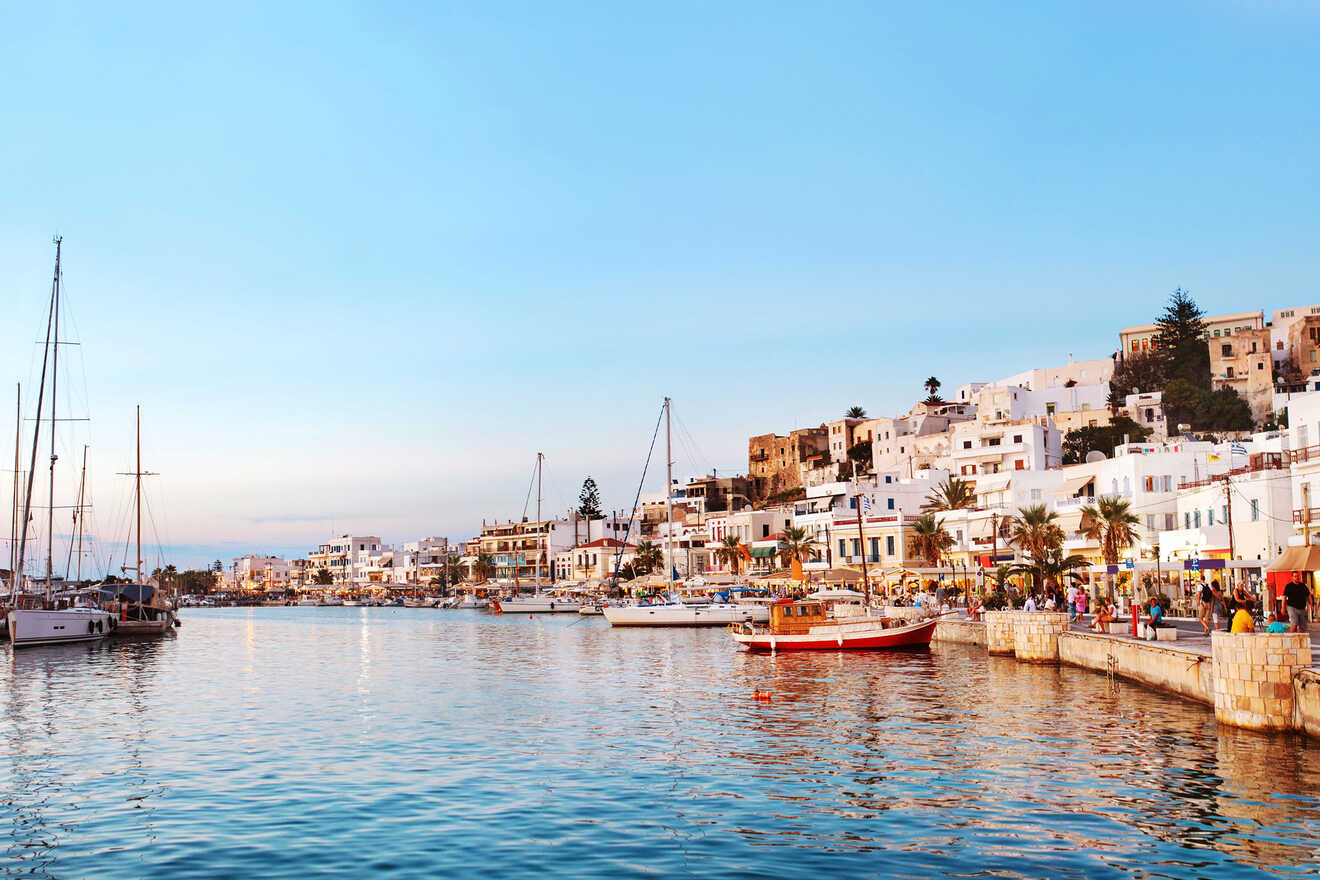  A vibrant coastal town with white buildings and colorful accents, bustling with activity at sunset, with boats docked along the water.