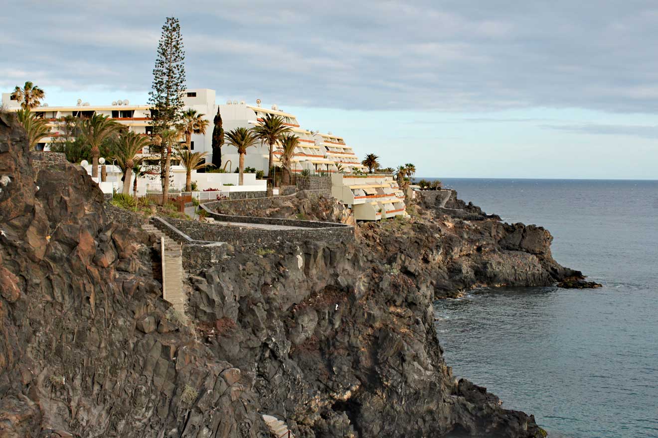 Oceanfront resort perched on a rugged cliff with palm trees and luxurious amenities, overlooking the tranquil sea