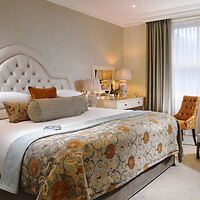 A luxurious hotel bedroom with an upholstered headboard, floral-patterned bed end, and classic decor accents