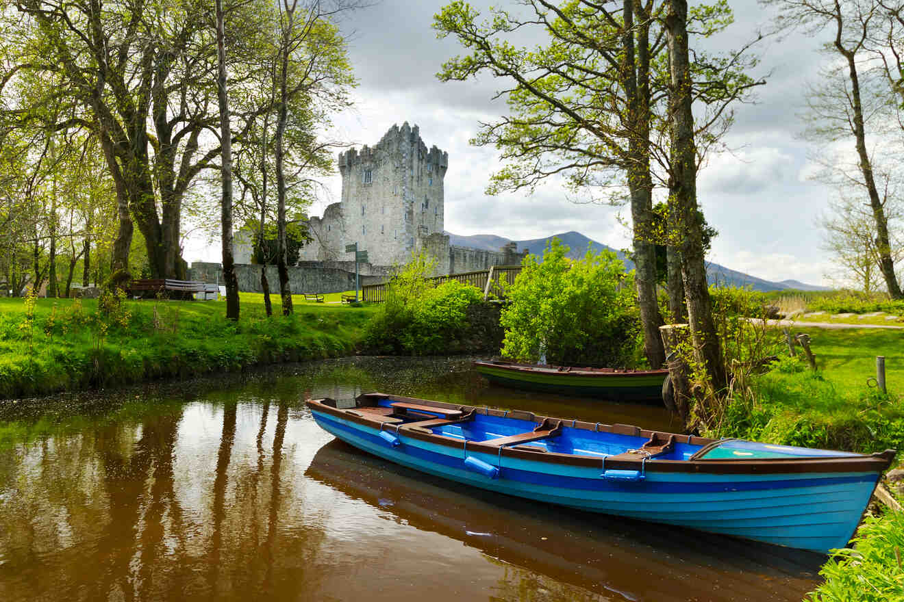 Serene landscape featuring a medieval castle by a river with moored blue rowboats in the foreground and lush greenery under a cloudy sky