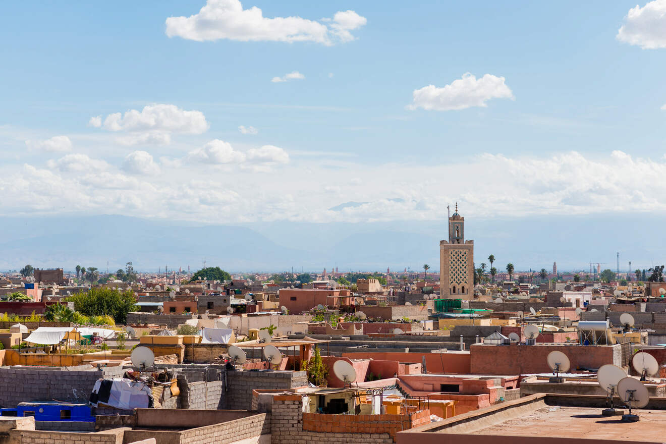 A panoramic view of Marrakech skyline showcasing traditional architecture with the Atlas Mountains in the backdrop under a clear blue sky.