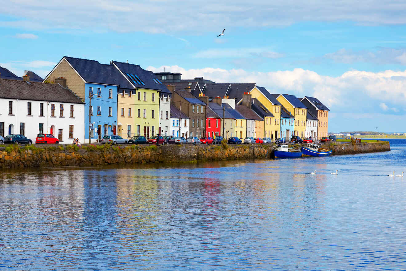 Colorful row houses along a calm waterfront with parked cars and a clear blue sky in a quaint coastal town.